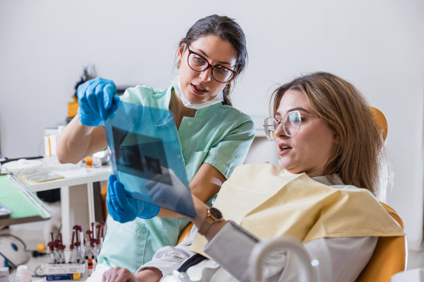 年轻的女牙医向病人展示全景牙科x光片-库存照片图片下载