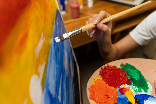 近距离的女性手艺术家在暗室温暖的光工作，用刷子和不同的丙烯酸颜料绘画。作为艺术概念的女艺术家在创作工作室的画布上作画图片下载