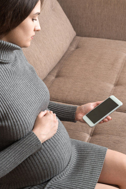 坐在沙发上用智能手机摸肚子的孕妇。一个女人在手机上发短信图片下载
