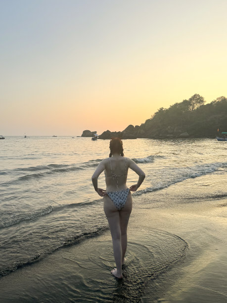 在印度果阿的冬季假期里，一名印度妇女穿着两件式泳衣(比基尼)，在日落时分走进热带Palolem海滩的浅水区，这是一幅难以辨认的照片图片下载