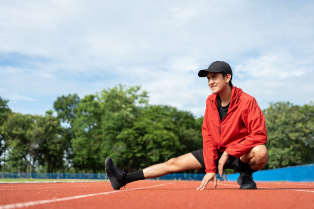 年轻的亚洲男子穿着运动服在户外跑步。印度男子在体育场跑道上跑步前伸展腿的照片。训练运动员在户外运动的概念。图片下载