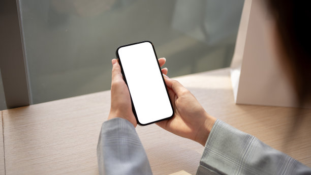 一个女人在室内的桌子上使用她的智能手机的特写照片。一个白屏智能手机模型。图片下载