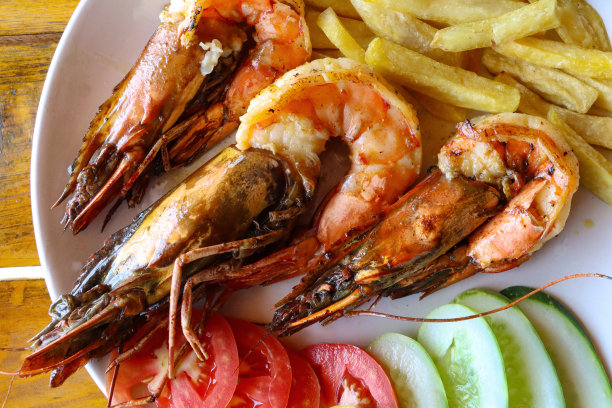 唐杜里王对虾的特写图片，新鲜脆的薯条片，与番茄和黄瓜片一起放在白色盘子里，餐厅餐桌背景，高架视图图片下载