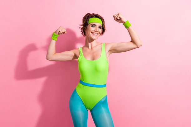 照片中冷静自信的女士穿着绿色运动紧身衣，举起拳头，显示肌肉空白，孤立的粉红色背景图片下载