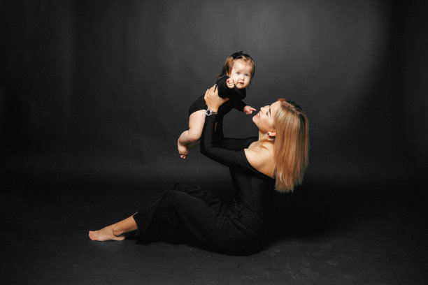 一位年轻的母亲微笑着抱着她蹒跚学步的女儿的特写照片，背景是黑色的。快乐的母子关系。妈妈正在和小女孩玩图片下载