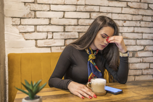 可爱的女孩一边坐在自助餐厅喝咖啡，一边读着令人不安的信息。图片下载