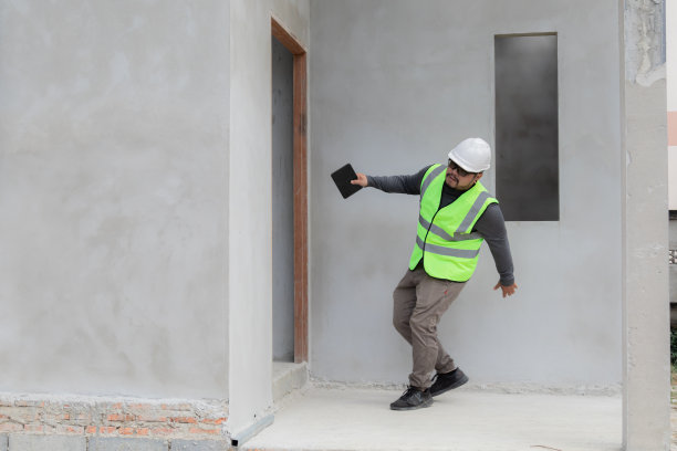 亚洲经理、工头或工程师在工地未完工的水泥事故中滑倒，施工监理头戴白色头盔手持牌匾摔倒在地，保险和安全观念图片下载