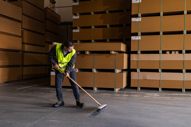 患有唐氏综合症的年轻人在工厂、仓库扫地的照片。残疾工人的概念，在工作场所的支持。图片下载