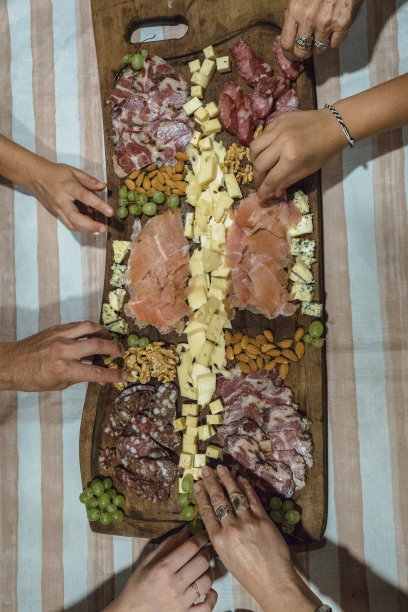 前视图。手从熟食板上拿着冷肉、奶酪、坚果和葡萄。分享食物。垂直的照片。图片下载