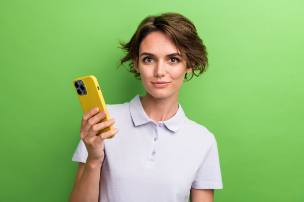 照片中的年轻学生年龄的女孩穿着时尚的紫色t恤polo使用智能手机支付租金孤立的绿色背景图片下载