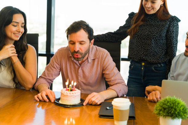 英俊的商人正在吹同事刚给他买的生日蛋糕上的蜡烛图片下载