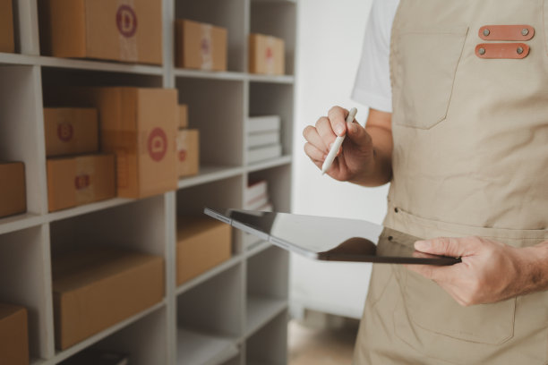 平板电脑被用来做各种各样的活动来促进商店的销售，网上商店的老板根据在线销售网站的订单将产品包装成包裹盒。图片下载