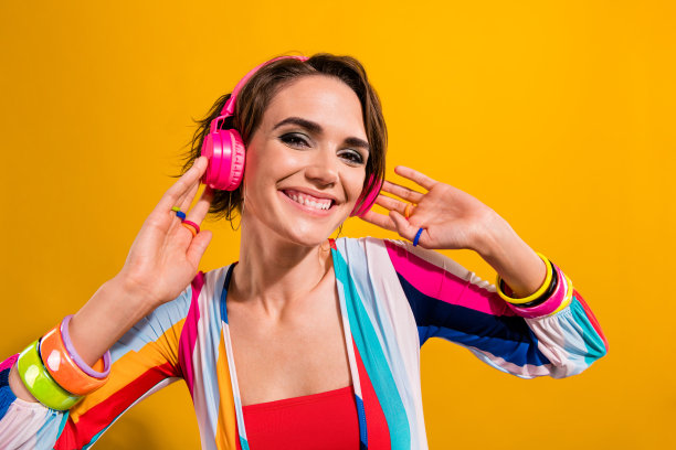 照片中的美女穿着条纹西装，听着摇滚音乐，耳机孤立的黄色背景图片下载