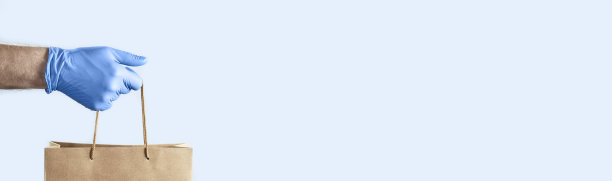 戴着蓝色橡胶手套的手拿着一个纸袋。带复印空间的照片。大流行期间的安全概念。图片下载