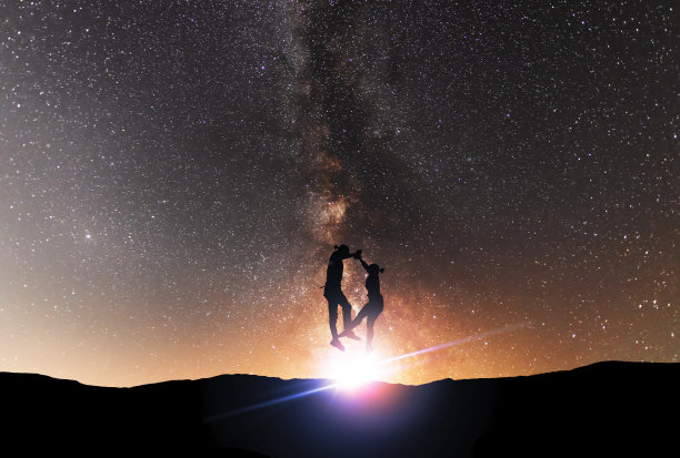 男人和女人的剪影在夜晚跳舞，在明亮的银河系背景上。图片下载