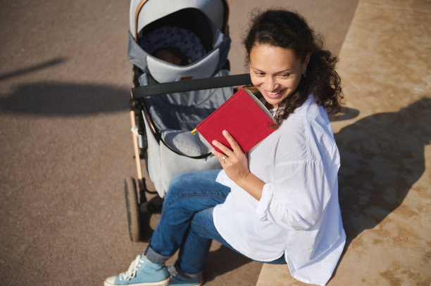 从上面看，真正的可爱的年轻母亲微笑着看着，享受户外读书图片下载