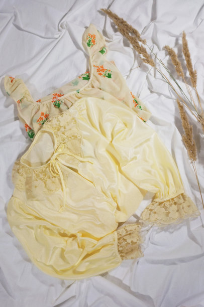 妇女的复古睡衣为家庭和睡眠。唯美复古的平面照片在白色的背景与野生植物。褶皱布料上的金色女孩睡衣。图片下载