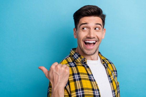照片中，一名穿着黄色格子衬衫、长着獠牙的男子露出大拇指，背部空白，孤立的蓝色背景图片下载