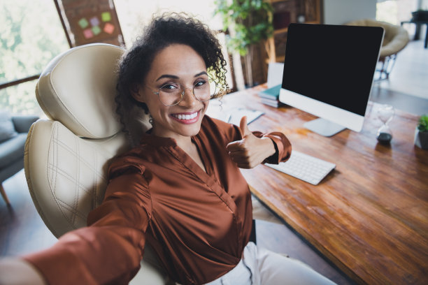 漂亮成功的女经纪人的照片坐在椅子上做自拍示范拇指向上腾空监视工作站室内图片下载