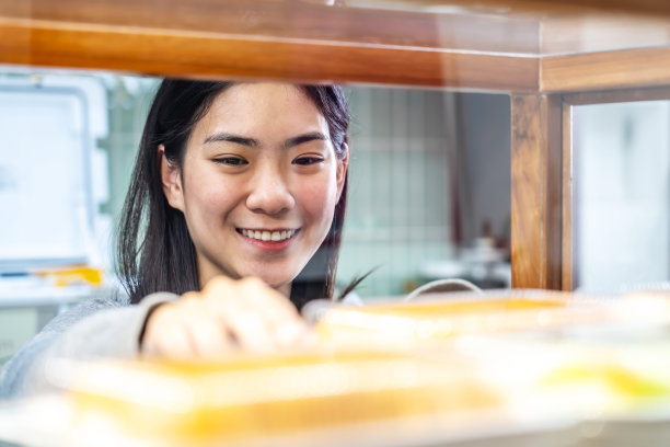 年轻漂亮的亚洲女工站在货架旁，整理新鲜的糕点或面包图片下载