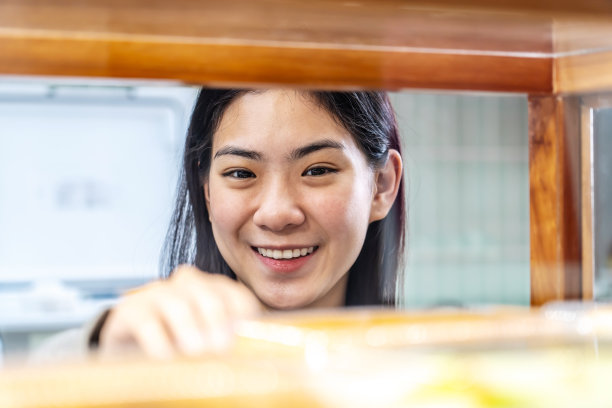 年轻漂亮的亚洲女工站在货架旁，整理新鲜的糕点或面包图片下载