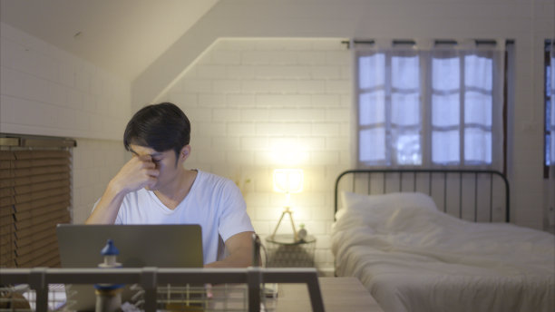 在家里加班的亚洲年轻人，通过吃药和喝水来缓解压力和头痛。图片下载