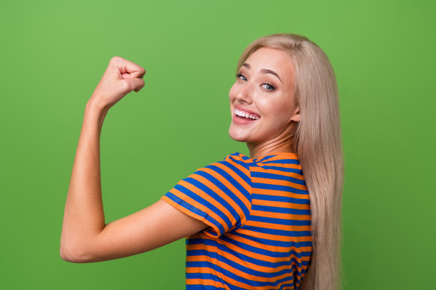 照片中，开朗积极的运动女孩穿着时髦的衣服，在绿色背景上显示出肌肉发达的手臂图片下载