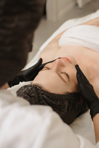 一个合格的按摩治疗师的女人的手按摩女性客户面部皮肤的俯视图。美容护理理念。垂直的照片。图片下载