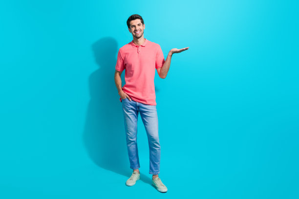 开朗的年轻英俊的黑发男子手持手掌的全身照片，在海蓝宝石色的背景上显得孤立无援图片下载