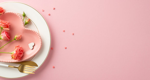 梦幻情人节的氛围:俯视图照片展示迷人的晚餐设置。心形的盘子，餐具，玫瑰，洒花和主题装饰在柔和的粉红色背景，文字或促销空间图片下载