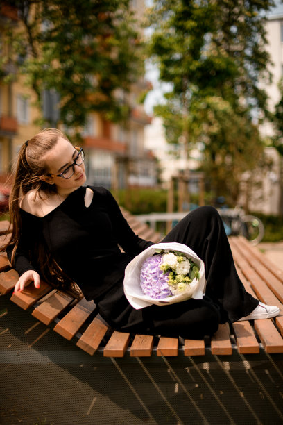 穿着漂亮时尚的女孩躺在长凳上，手里拿着精美的白色工艺纸花束图片下载