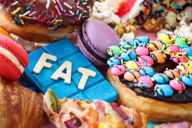 全画幅的木质字母拼写“脂肪”的甜味和咸味的垃圾食品，披萨片，羊角面包，光滑的环形甜甜圈，马卡龙，彩虹蛋糕片，爆米花，巧克力棒，重点前景，不健康的饮食理念图片下载