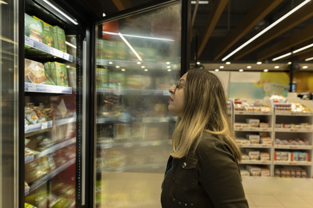 戴着圆眼镜、蓝头发的女人在商店里购物。她看着这些产品，想着该选什么。库存图片图片下载