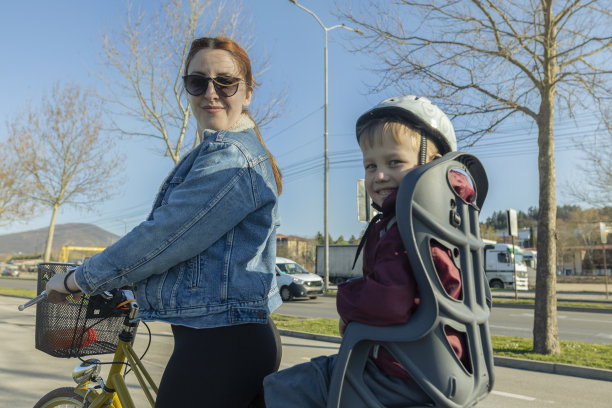红头发的单身母亲，骑着她儿子的自行车。蹒跚学步的孩子和妈妈一起骑自行车。休闲的衣柜里，她穿着一件蓝色牛仔夹克，日落时分，他们一起享受时光。美丽的春日里的亲密时光。库存图片图片下载