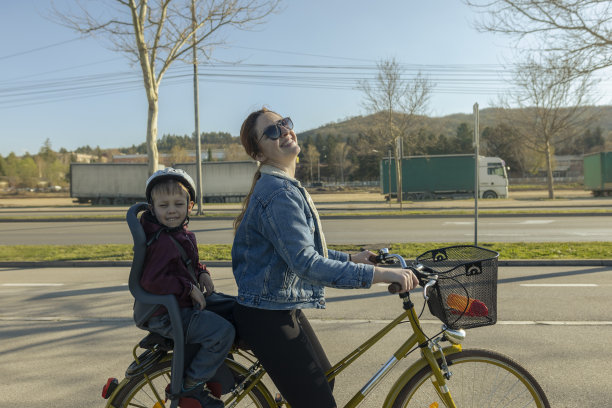 红头发的单身母亲，骑着她儿子的自行车。蹒跚学步的孩子和妈妈一起骑自行车。休闲的衣柜里，她穿着一件蓝色牛仔夹克，日落时分，他们一起享受时光。美丽的春日里的亲密时光。库存图片图片下载