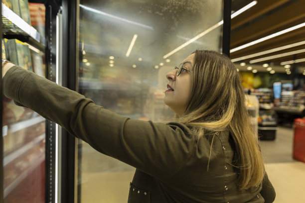 戴着圆眼镜、蓝头发的女人在商店里购物。她看着这些产品，想着该选什么。库存图片图片下载