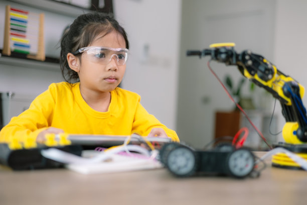 一个小女孩拿着一个机器人玩具坐在桌子旁图片下载