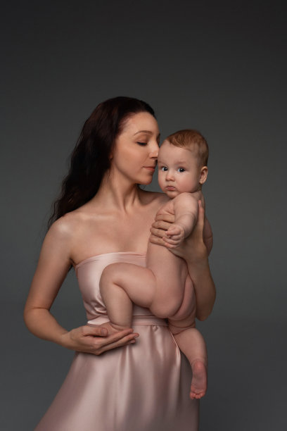 一名深色长发的年轻女子，穿着浅色的嬉闹裙，抱着一个看着照片的小男孩。一个在母亲怀里的孩子的特写肖像。暗的背景图片下载