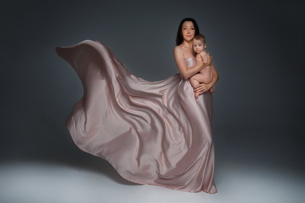 一名深色长发的年轻女子，穿着浅色的嬉闹裙，抱着一个看着照片的小男孩。一个在母亲怀里的孩子的特写肖像。暗的背景图片下载