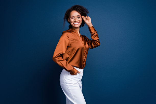 照片中可爱可爱的女人穿着棕色丝绸衬衫，手臂，手戴眼镜微笑孤立的蓝色背景图片下载