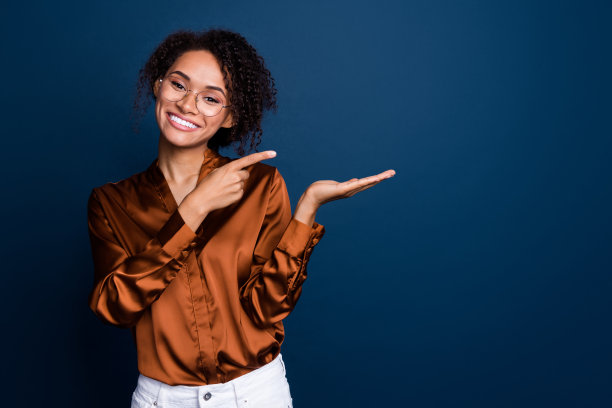 照片中可爱漂亮的女士穿着丝绸棕色衬衫，戴着眼镜，手臂露出手指，空白空间孤立的蓝色背景图片下载