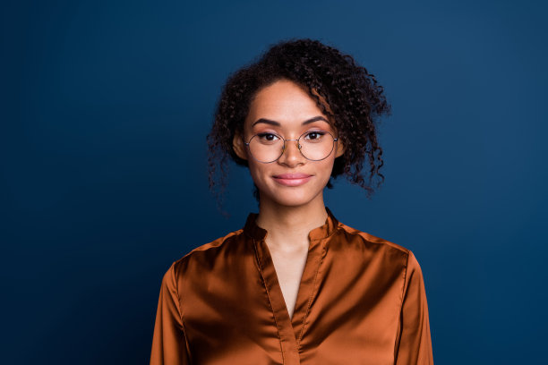 照片中可爱漂亮的女人穿着棕色丝绸衬衫，戴着眼镜，微笑着孤立的蓝色背景图片下载