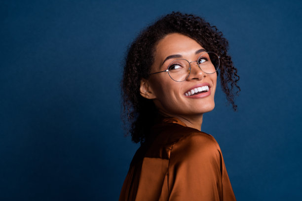 照片中开朗体贴的女人穿着棕色丝绸衬衫，戴着眼镜，回头望空，孤立的蓝色背景图片下载