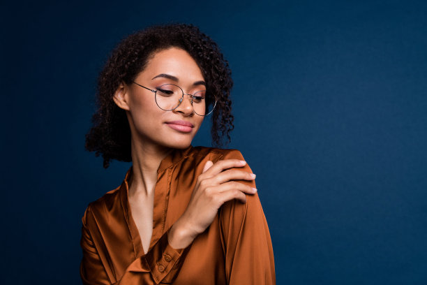 照片中甜美积极的女人穿着棕色丝绸衬衫，戴着眼镜，拥抱自己，空白的空间孤立的蓝色背景图片下载