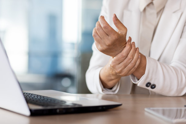 一张特写照片，一位资深女商人坐在办公室的桌子前，按摩着她疲惫的手图片下载