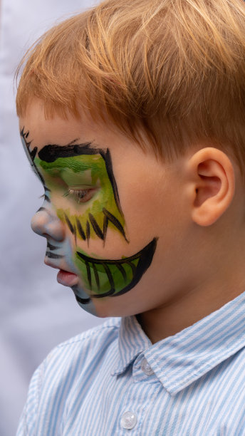 一个金发男孩的脸，脸上涂着绿色的颜料。水彩画，画孩子脸上的龙。图片下载