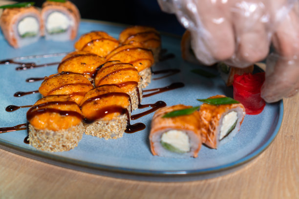 在餐厅的厨房里，厨师端着一盘烤寿司卷，上面放着姜和芥末。图片下载