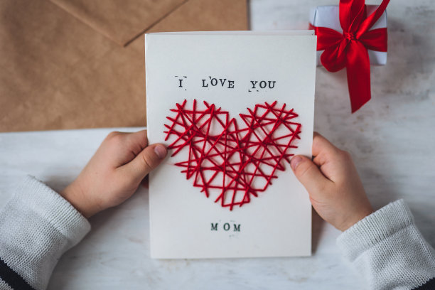 儿童工艺的概念，母亲节的手工礼物。小男孩手里拿着绣着心形的手工卡片，上面印有“我爱你，妈妈”的字样。儿童休闲活动，手工艺品图片下载
