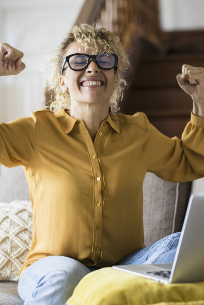 快乐兴奋的女人坐在家里的沙发上阅读信息，看着设备屏幕使用电脑。庆女感到满意的积极情绪带上了好帖和获奖通知图片下载