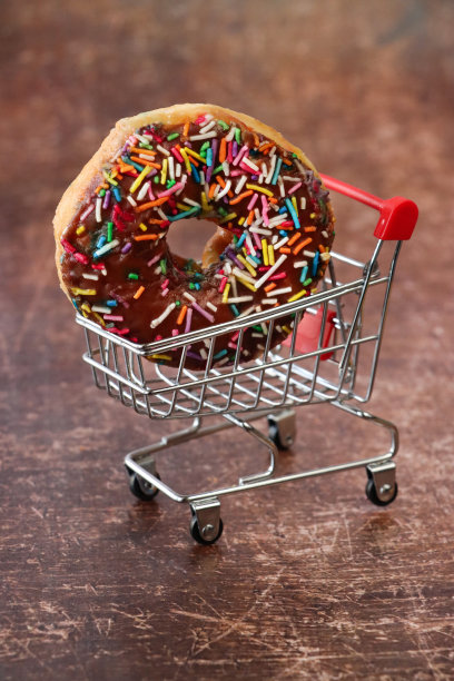个人特写，微缩釉面圈，购物车模型，五彩装饰的巧克力釉面甜点，成百上千的糖屑，不健康的食品零食，棕色背景，重点在前景图片下载